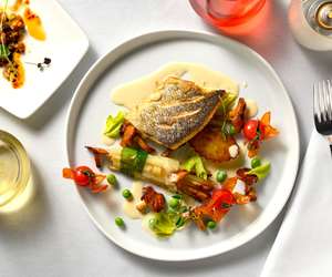 Pan seared Bronzino, white asparagus bundle, pomme fondante, cherry tomatoes, chanterelles, English peas, white wine sauce